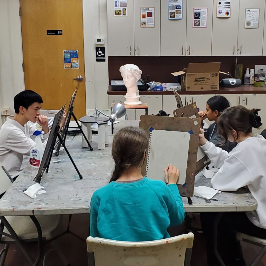 seated students draw a still life image