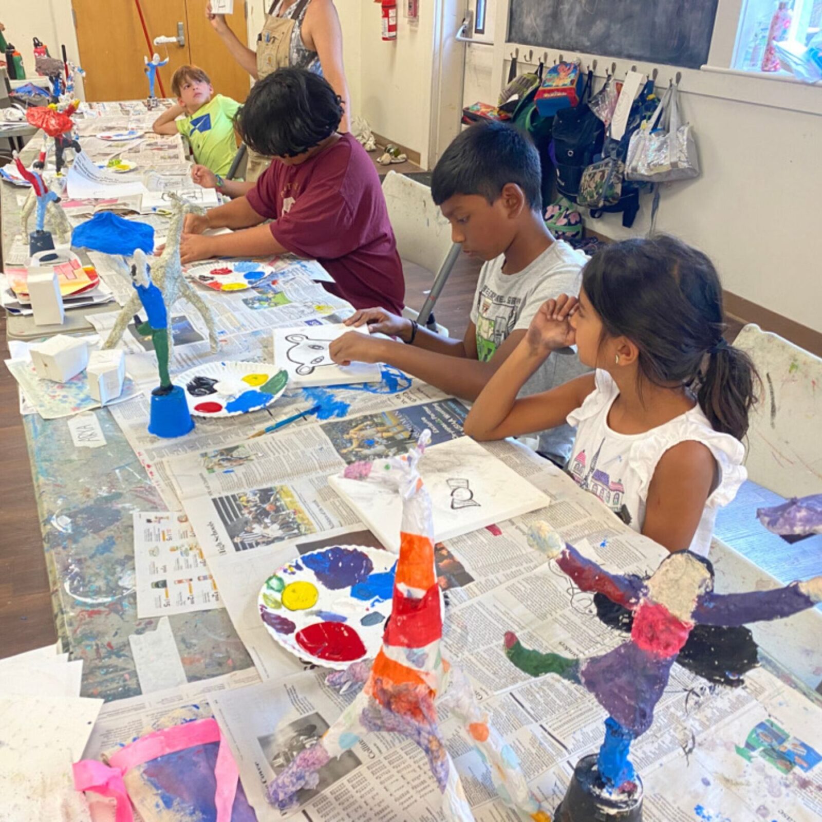 Three students painting colorful sculptures