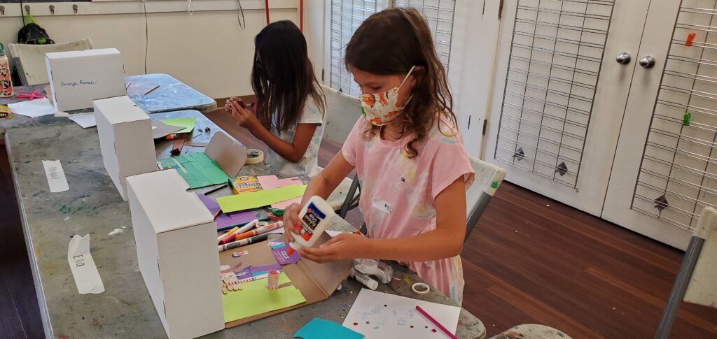 Young girl in pink shirt glues colored paper down to art project.