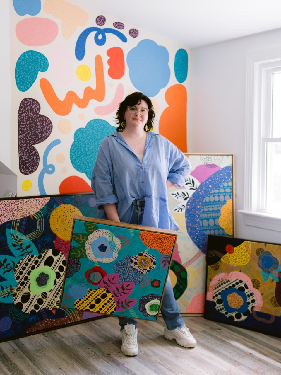 Photo of artist Fiona Clark with her paintings.