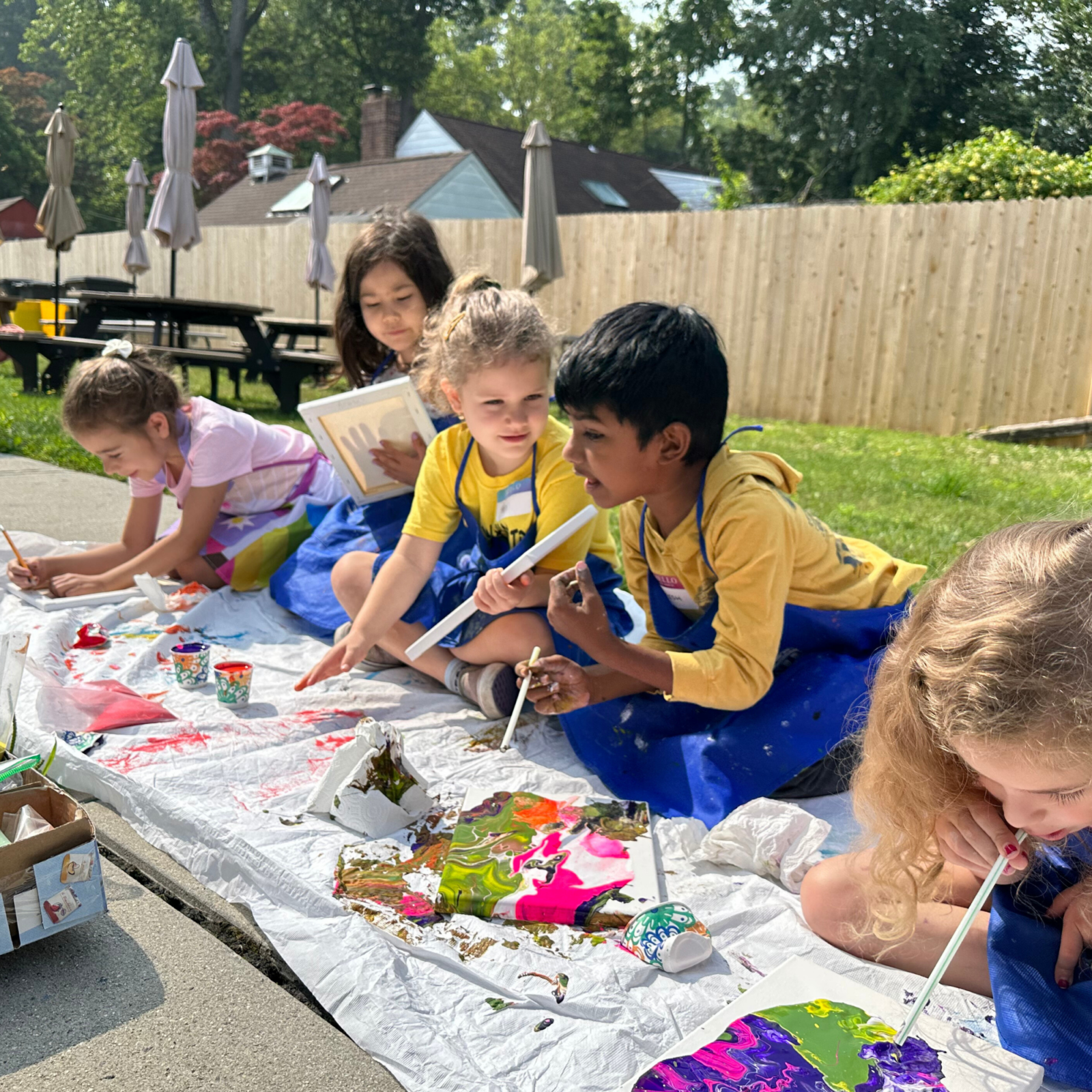 5 children making paint pouring canvas art outside