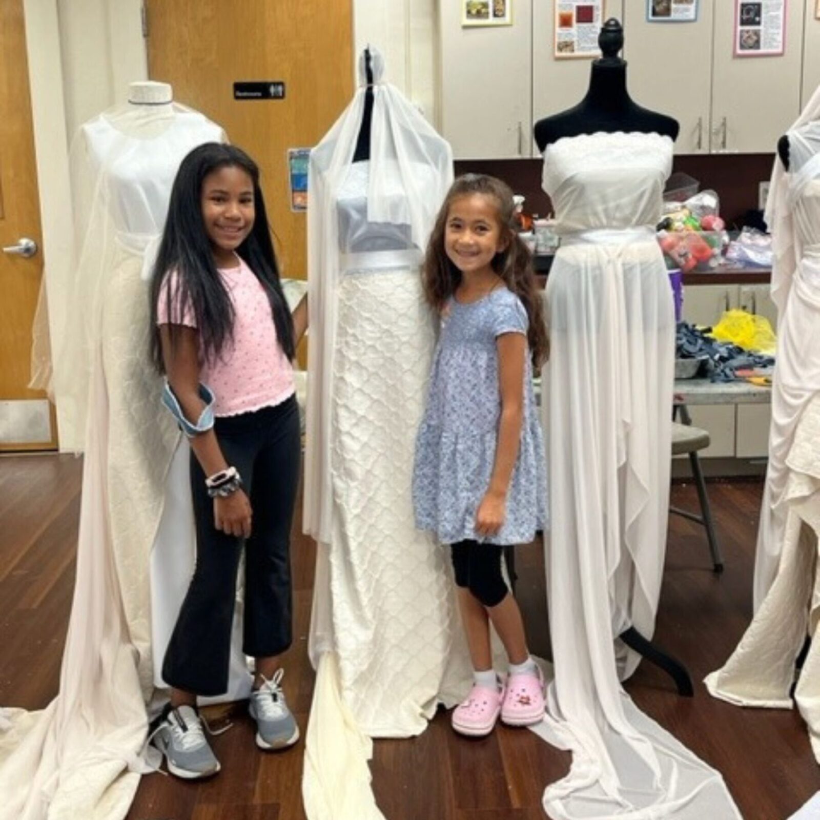 2 girls with 3 mannequins with white dress deigns