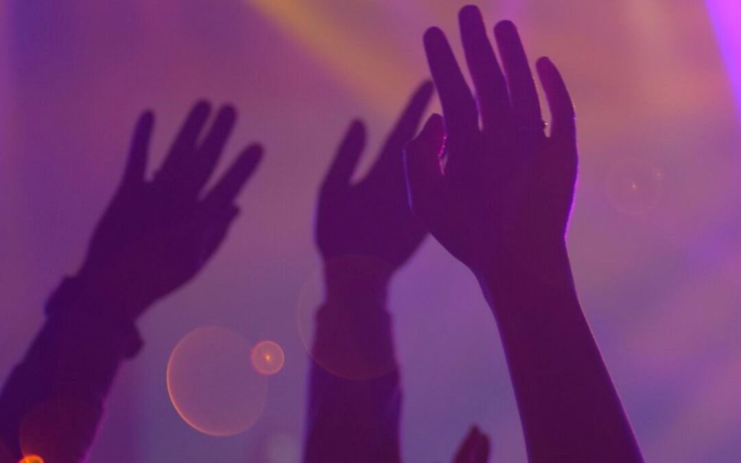 Hands raised in purple light with blurry yellow lights in background